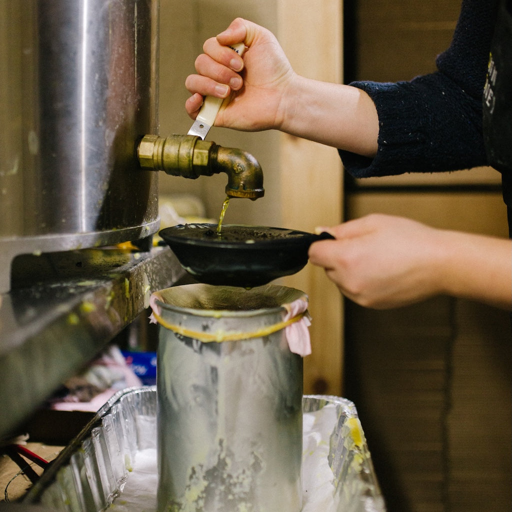 Person pouring beeswax from a metal container using a brass faucet.