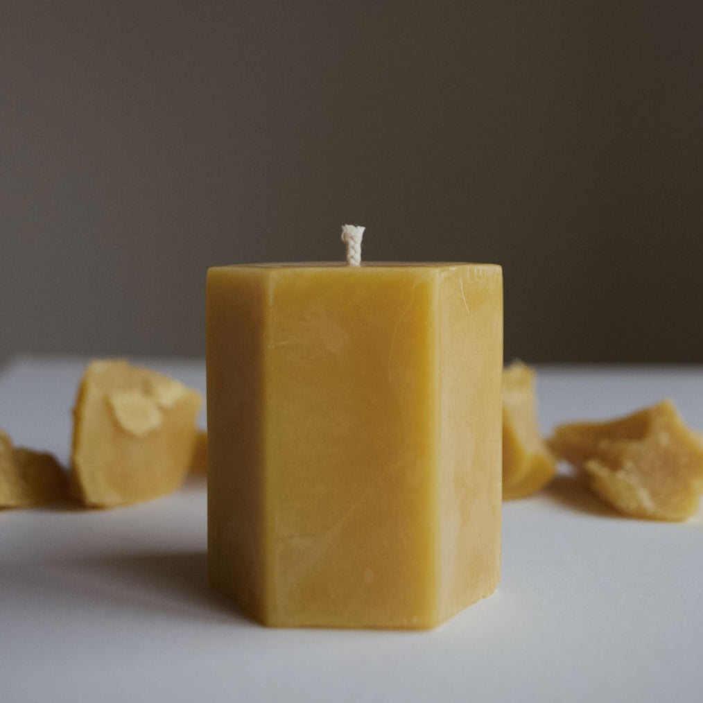 Hexagonal beeswax candle with honeycomb pieces on a neutral background
