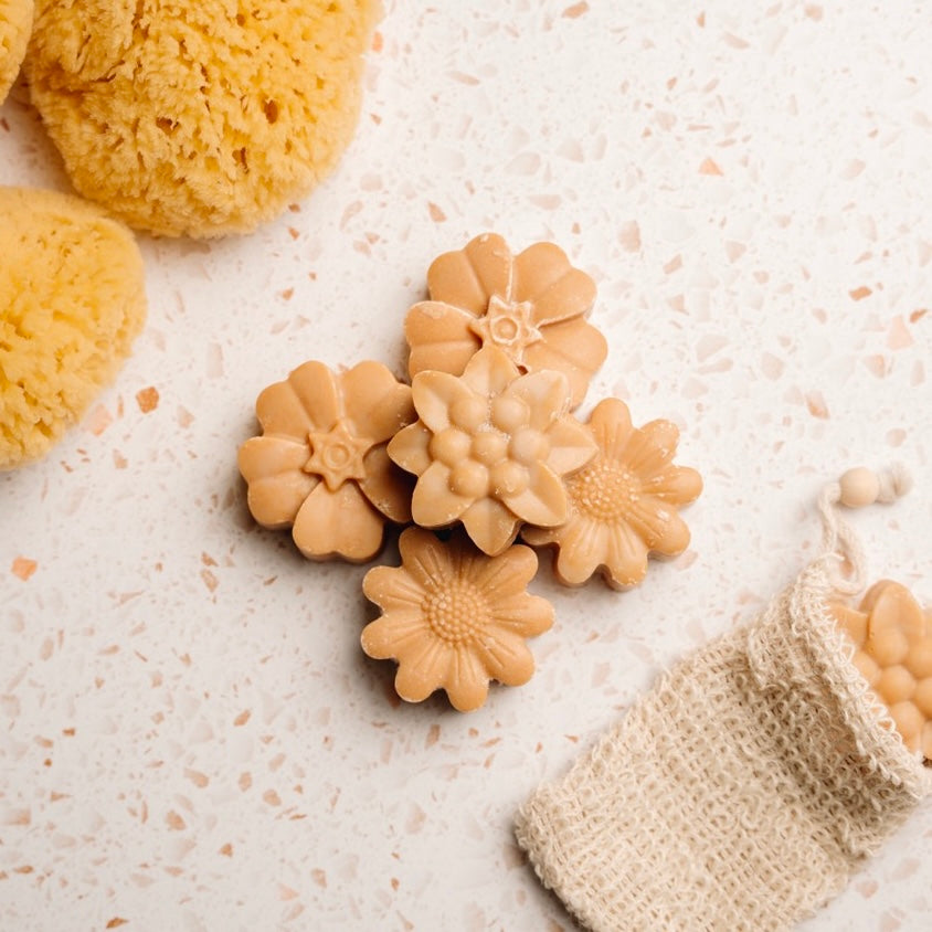 Flower-shaped soap bars on a textured surface with a natural sponge.