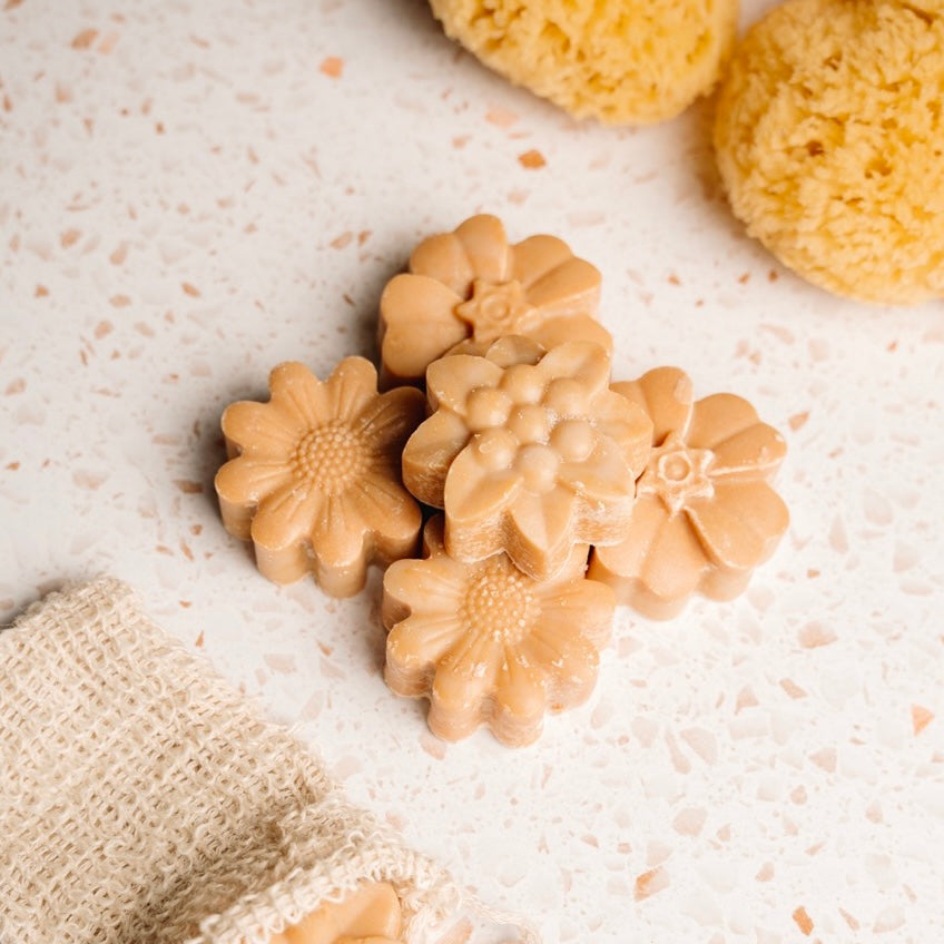 Flower-shaped natural soap bars on a textured surface with natural sponges.