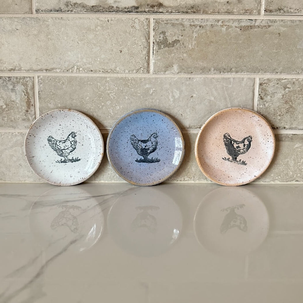 Three ceramic plates with chicken illustrations on a tiled wall.