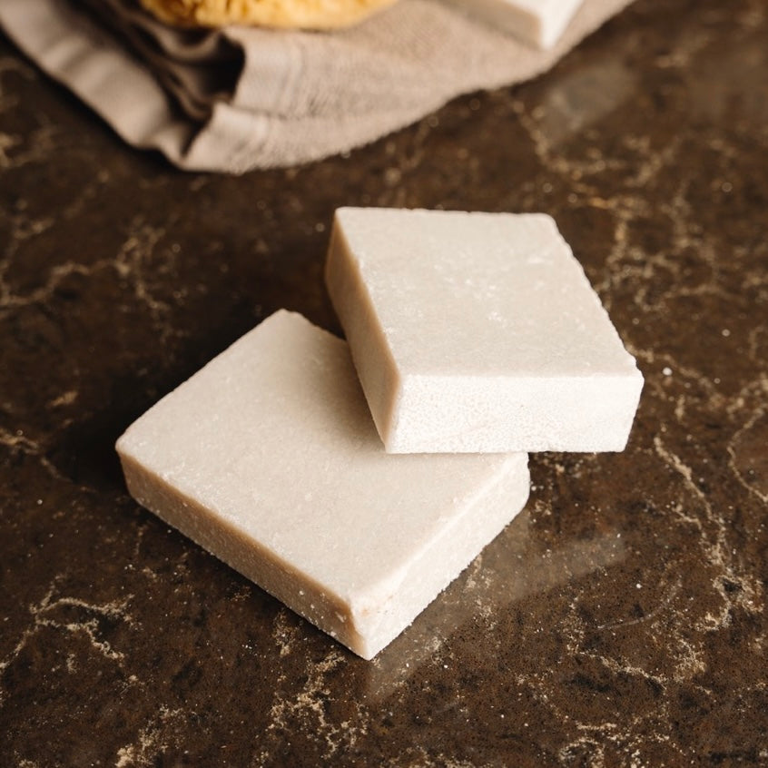 Two square pieces of white sea salt soap on a dark marble surface.