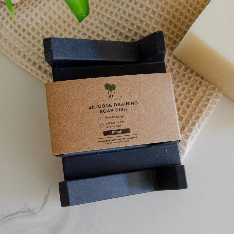 Black silicone draining soap dish with cardboard packaging on a textured surface.