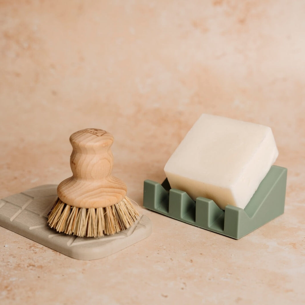 Green soap bar dish near brush on stone.